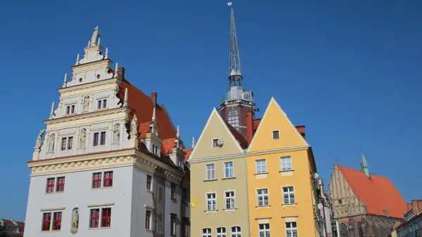 Kolorowe kamienice i wieża kościelna na rynku w Nysie pod błękitnym niebem.
