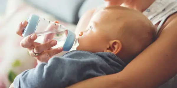 Mama próbuje nakarmić butelką dziecko, które nie chce pić wody.