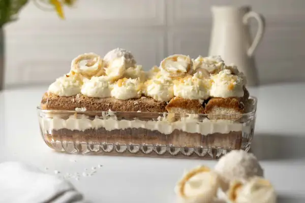 Ein Raffaello Tiramisu in einer Glasform, geschichtet mit Löffelbiskuits, Creme und Kokosraspeln. Obenauf dekorative Kokospralinen.