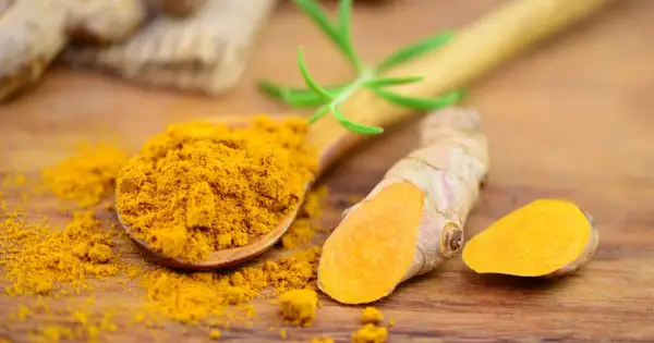 Kurkuma-Pulver auf einem Holzlöffel und frische Wurzeln. Kurkuma kann bei Durchfall helfen.