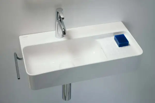 Elegancka, mała umywalka wisząca z chromowaną baterią i kostką niebieskiego mydła.