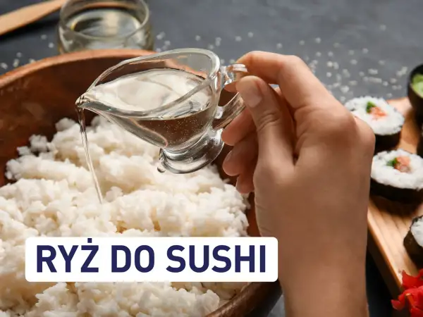 Dłoń wylewa płyn z sosjerki na ryż do sushi. Obok widać gotowe rolki sushi.