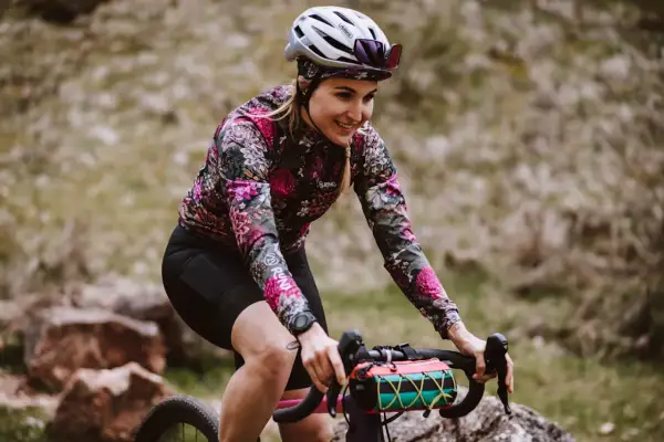 Uśmiechnięta rowerzystka w kwiecistej bluzie pokonuje kolejne kilometry. Dziś czeka ją 50 km na rowerze po malowniczych terenach.