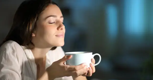 Kobieta z zamkniętymi oczami wdycha aromat napoju. Może to być kawa lub napar z ziół na pobudzenie.