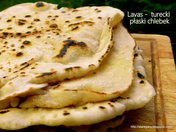 Stos puszystego, lekko przypieczonego **chleba tureckiego** na drewnianej desce. Idealny do dipów i jako dodatek do dań.