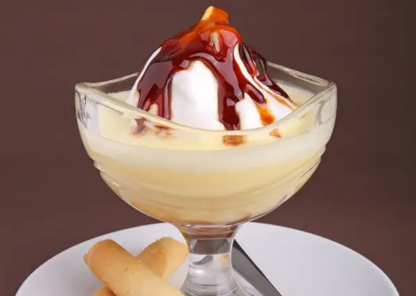 Un dessert crémeux avec une meringue nappée de caramel, servi dans un verre, évoquant des iles flottantes. Des biscuits fins l'accompagnent.