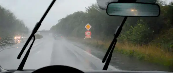 Conduire sous la pluie sur une route mouillée, avec des essuie-glaces en action et un panneau de rappel de vitesse 110.