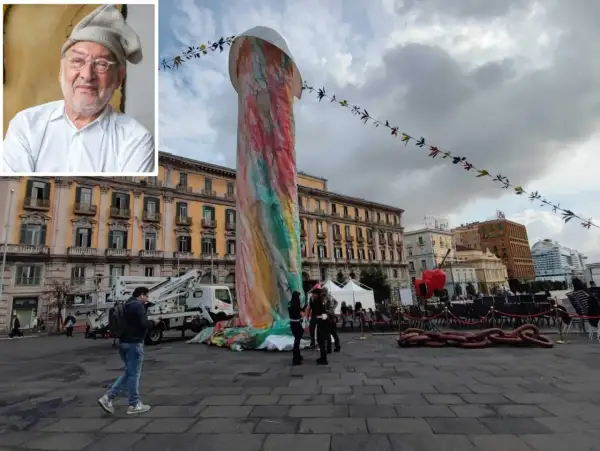 Ritratto di artista con inquadratura di una colorata statua di Pulcinella a Napoli, in piazza, con edifici storici sullo sfondo.
