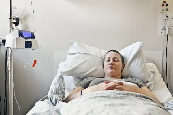 Kobieta zmagająca się z rakiem piersi z przerzutami odpoczywa w szpitalnym łóżku, podłączona do pompy infuzyjnej.