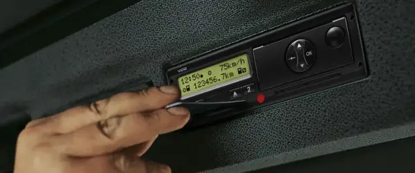 Une main insère une carte dans un tachygraphe intelligent VDO affichant 75 km/h et 23456.7 km.