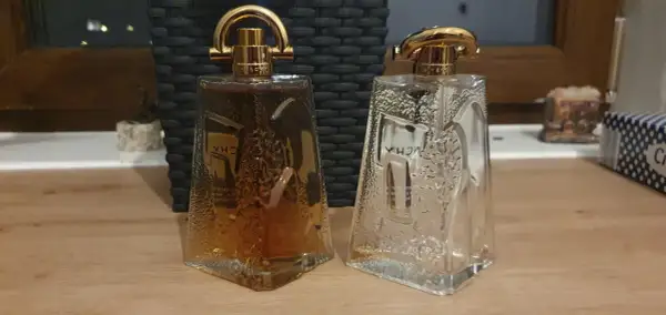 Dwie butelki Givenchy Pi: jedna pełna bursztynowego płynu, druga pusta, obie z ozdobnymi złotymi nakrętkami.