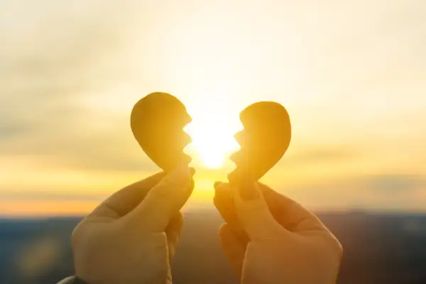 Mani che tengono due pezzi di un cuore spezzato contro un tramonto dorato. Un sentimento di nostalgia, non riesco a lasciarti andare.