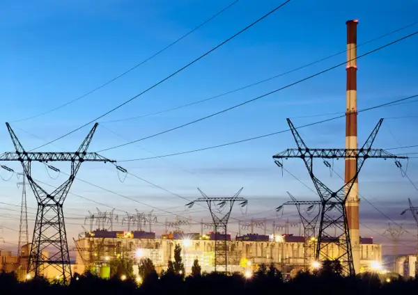 Elektrownia z kominem i liniami wysokiego napięcia. W tle widać budynki zakładu, a nad nimi niebo o zmierzchu. To obraz, który może kojarzyć się z opłatą kogeneracyjną.