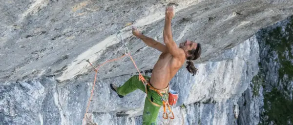 Alexander Huber klettert an einer steilen Felswand, sein Körper angespannt, die Hände greifen nach kleinen Vorsprüngen.