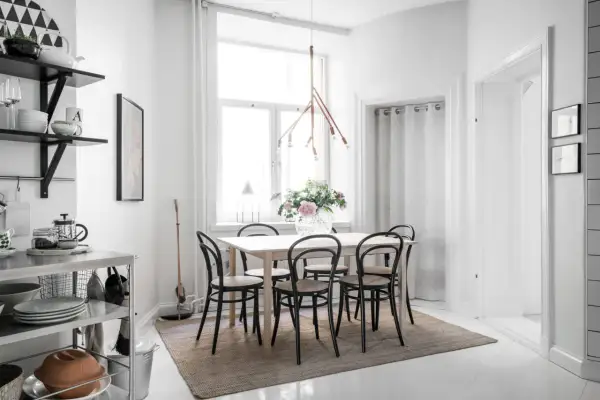 En ljus och mysig matplats med ett träbord, svarta stolar och en vacker blomsterbukett. En taklampa i trä ger ett varmt sken.