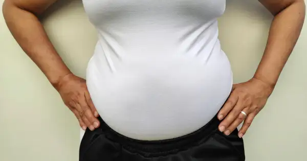 Kobieta w białej koszulce i czarnych spodniach, z rękami na biodrach. Nie jestem gruba, ale mam duży brzuch.