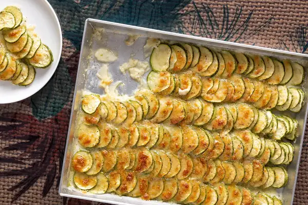 Fette di zucchine al forno con mozzarella filante, disposte in file ordinate in una teglia, pronte per essere gustate.
