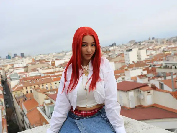 Joven con cabello rojo vibrante, como una rosa encendida, posa sobre tejados urbanos.
