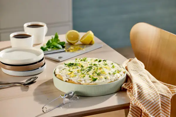 En krämig tiramisu limoncello, garnerad med citronzest och persilja, står på ett bord med kaffe och citroner.
