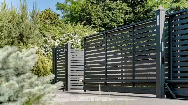 Nowoczesne, ciemnoszare ogrodzenie z przesuwną bramą i furtką. W tle bujna zieleń. Idealne, by sprawdzić wysokość ogrodzenia dla psa przepisy.