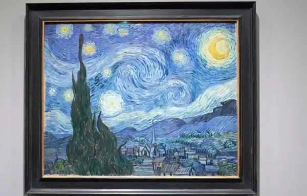 Van Gogh's blaues Bild zeigt einen wirbelnden Sternenhimmel über einem Dorf. Zypressen ragen empor, Sterne leuchten, der Mond strahlt.