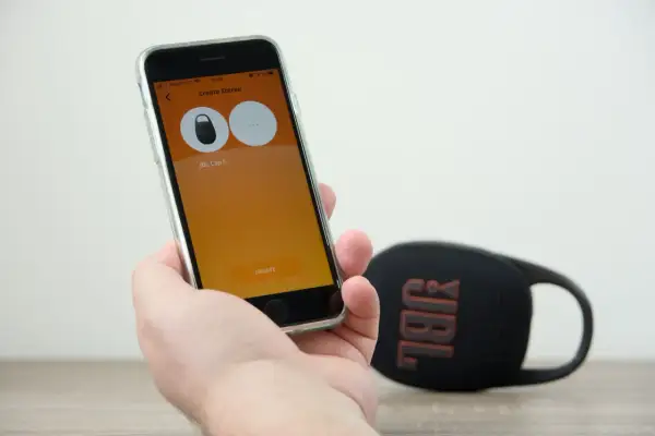 Sprawdzanie, czy słuchawki bezprzewodowe JBL działają z iPhone. Na ekranie telefonu widać aplikację do tworzenia stereo z głośnikiem JBL Clip 5.