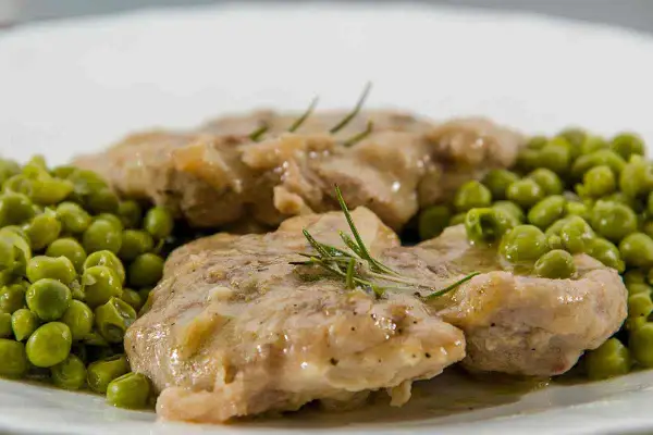 Ossobuco con piselli, un piatto succulento con carne tenera e piselli freschi, guarnito con rosmarino.