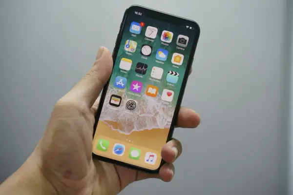 Dłoń trzyma iPhone'a z widocznym ekranem głównym. Chcesz wiedzieć, jak wyłączyć wibracje w iPhone? Wystarczy wejść w Ustawienia.