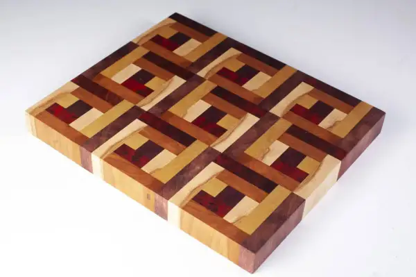 A beautiful diy cutting board with an intricate geometric pattern made from various wood types and red accents.