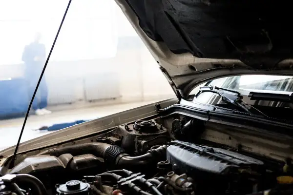 Bilmotor med öppen huv. En person står i bakgrunden, kanske en mekaniker som undersöker igensatt luftfilter symtom.