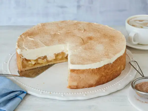 Saftige Apfel Schmand Torte mit Zimt bestäubt, bereit zum Servieren neben einer Tasse Kaffee.