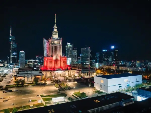 Warszawski Pałac Kultury i Nauki rozświetlony na czerwono, niczym scena przed wielkim koncertem. W tle nocna panorama miasta.