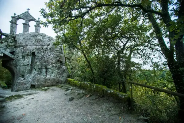 Antigua ermita rupestre de San Pedro de Rocas, con su estructura de piedra y arcos, rodeada de vegetación frondosa.