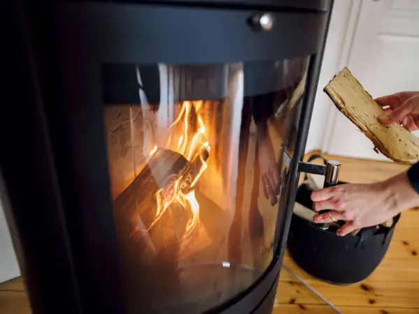 Hände legen Holzscheite in einen modernen Kamin, der brennt. Informieren Sie sich, welche Kamine noch erlaubt sind.
