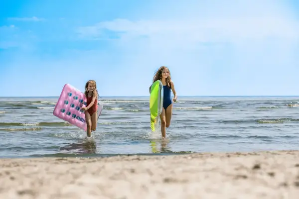 Zwei Mädchen rennen lachend mit Luftmatratzen über den mecklenburgische Seenplatte strand ins Wasser.