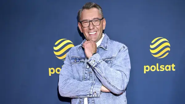 Uśmiechnięty Darek Stolarz w dżinsowej kurtce, z podpartą brodą, na tle logo Polsatu.