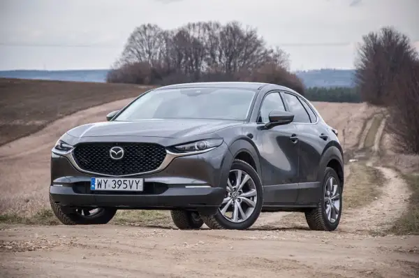 Szary Mazda CX-30 na polnej drodze. Wady tego modelu to m.in. ograniczona widoczność i twarde zawieszenie.