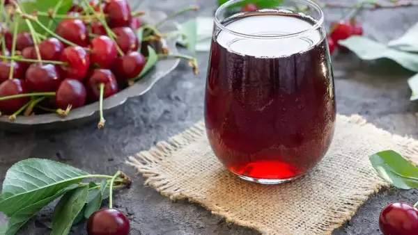 Szklanka orzeźwiającego soku z wiśni, obok miseczki pełnej świeżych owoców. Idealny na lato, prosty sok z wiśni przepis.