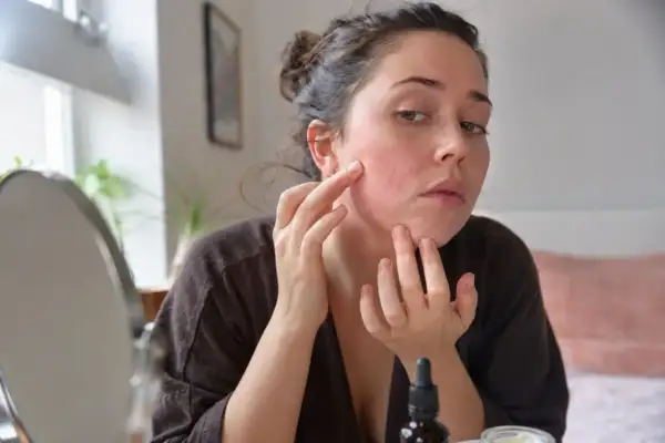 Kobieta bada zaczerwienioną skórę twarzy, sprawdzając możliwe retinol efekty uboczne.