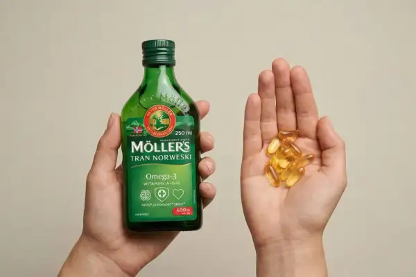 Dłoń trzyma butelkę Möller's Tran Norweski, a druga dłoń garść kapsułek z omega-3.