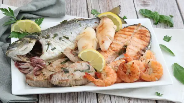 Un piatto invitante di grigliata di pesce: orata intera, tranci di salmone, gamberi, calamari e tonno, guarnito con limone e prezzemolo.