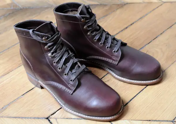Bottes en cuir brun foncé, parfaites pour reconnaître le cuir gras. Le bois du parquet reflète la lumière sur le cuir.