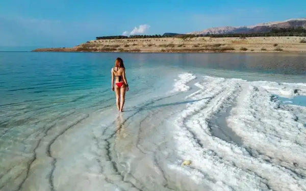 Kobieta w czerwonym bikini stoi na brzegu Morza Martwego, otoczona kryształami soli.