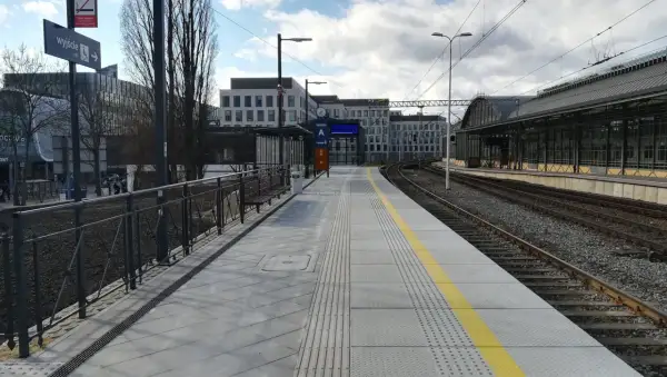 Peron 6 na dworcu Wrocław Główny, z którego odjeżdża pociąg. Nowoczesny peron z żółtym pasem bezpieczeństwa i budynkami w tle.