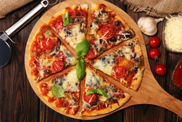 Pyszna pizza z pomidorkami i bazylią, obficie posypana serem do pizzy. Obok czosnek, pomidorki i sos.