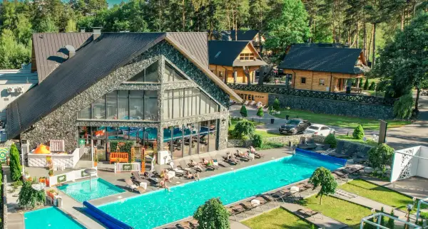 Hotel Bacówka Radawa: basen, leżaki i drewniane domki w otoczeniu lasu.