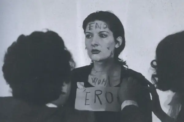 Marina Abramović w performansie "Rhythm 0" z napisem "END" na czole i "WOMAN ERO" na klatce piersiowej.