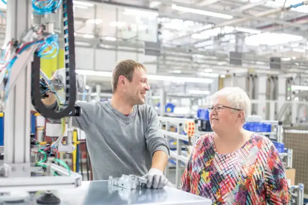 Zwei Kollegen in einer Fabrikhalle, die über ihre Arbeit sprechen. Vielleicht diskutieren sie, wie wird man Betriebsrat, um die Arbeitsbedingungen zu verbessern.