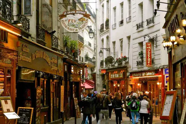 Callejuela parisina con restaurantes y gente paseando, evocando un ambiente de barrio latino en París.