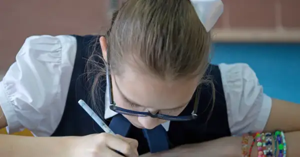 Dziewczynka w okularach ćwiczy grafomotorykę, pisząc długopisem.